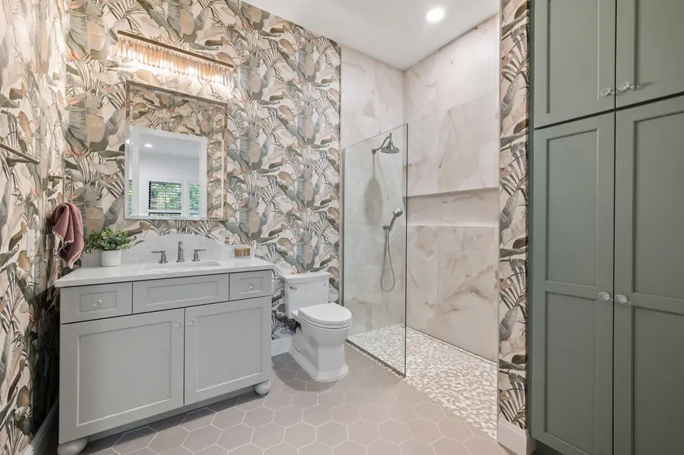 Guest bathroom designed by Zen Reno & Design in St. Augustine, FL, featuring statement botanical wallpaper, custom cabinetry, warm sage built-ins, and artisan tile details for a distinctive and personality-filled space.