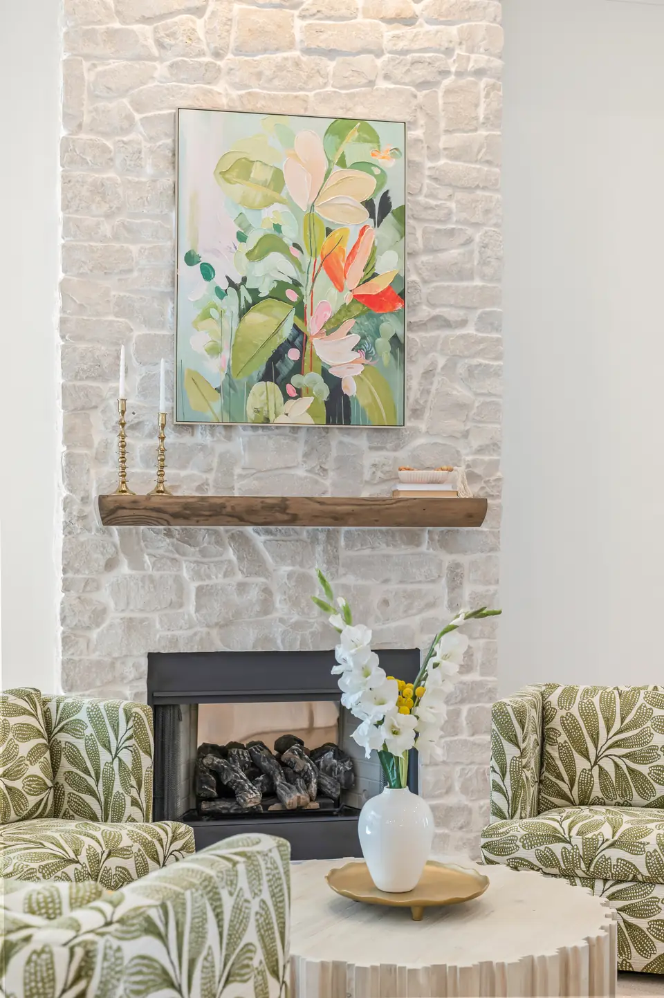 Living room designed by Zen Reno & Design in St. Augustine, FL, featuring botanical patterned accent chairs, a custom stone fireplace, statement artwork, and natural textures that bring warmth and personality to the space.